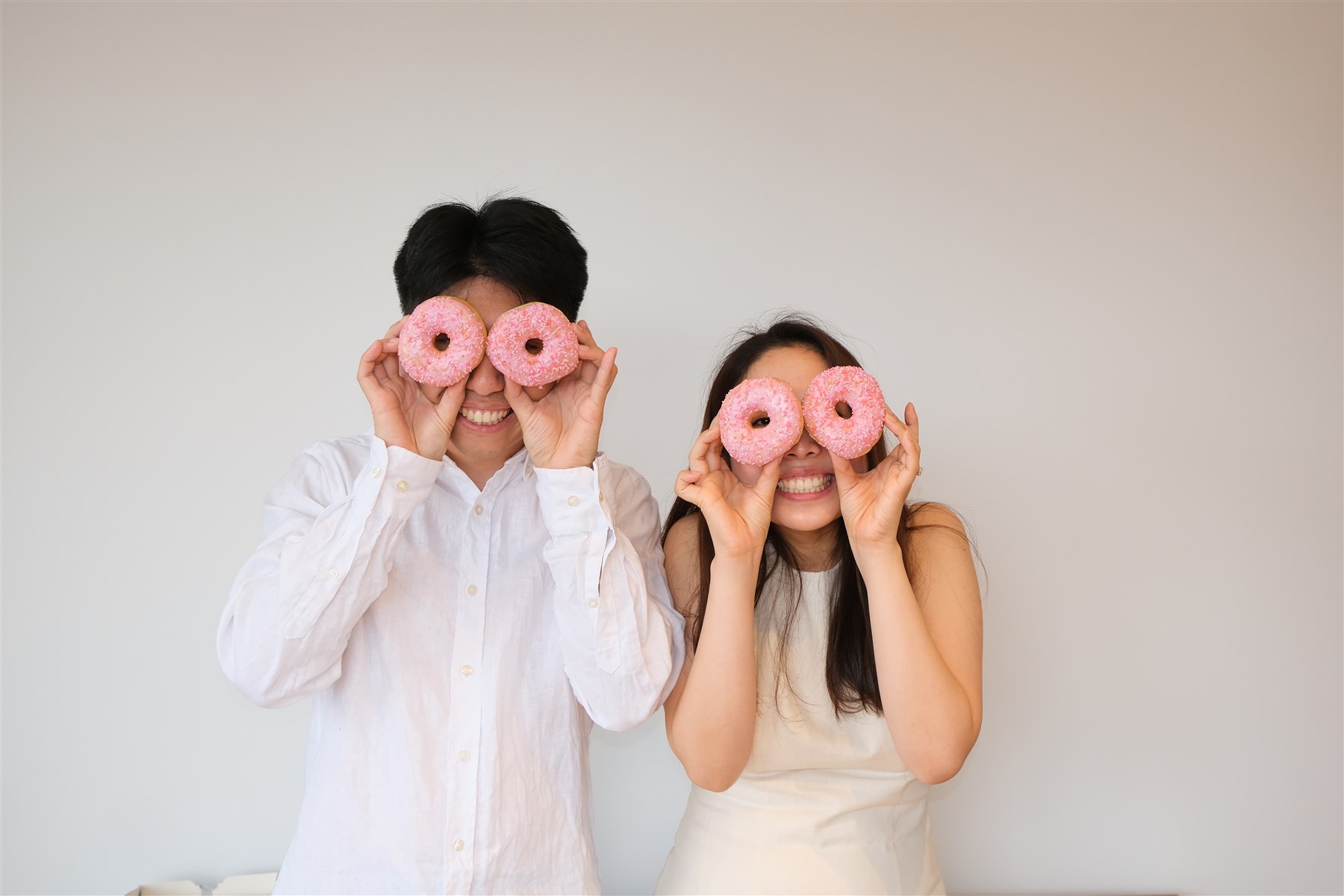 Shawn and Hitomi holding pink doughnuts over their eyes
