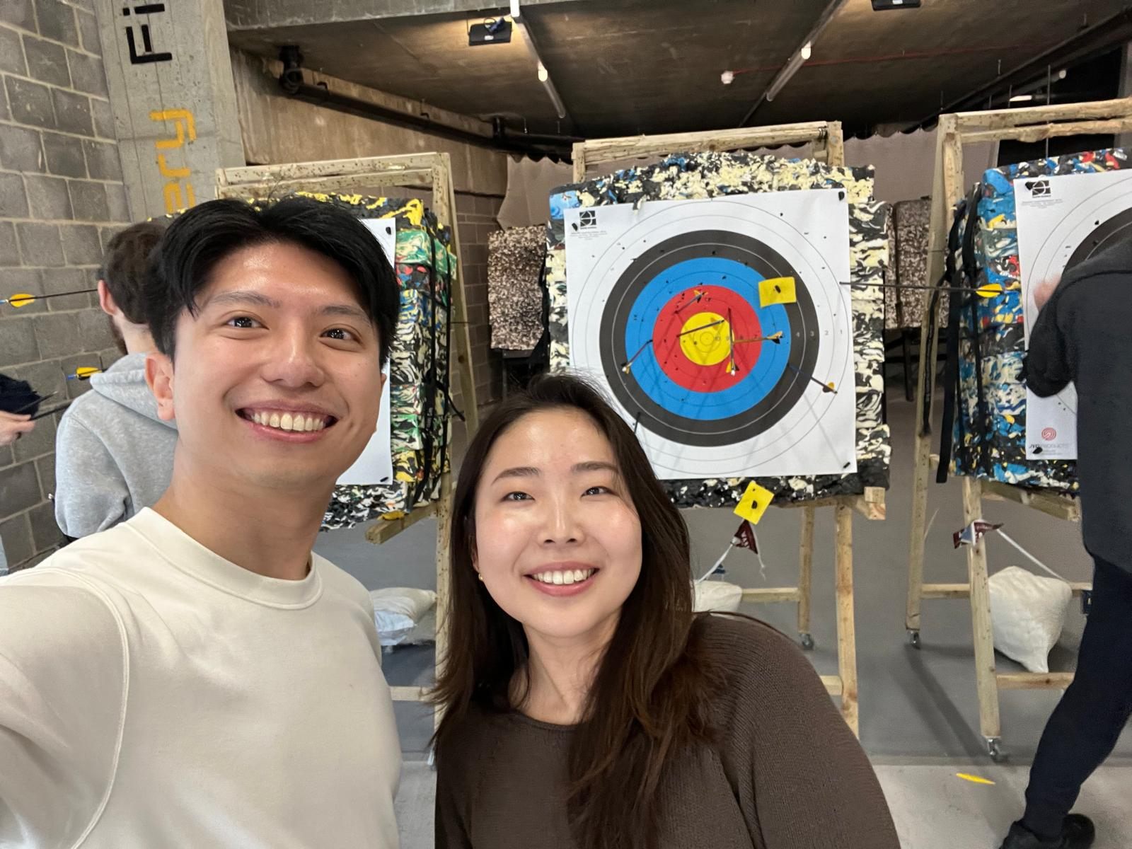 Shawn and Hitomi smiling beside targets at an archery range