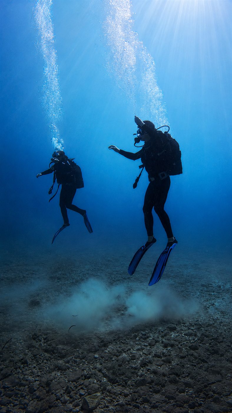 Two scuba divers swimming in sunlit blue water